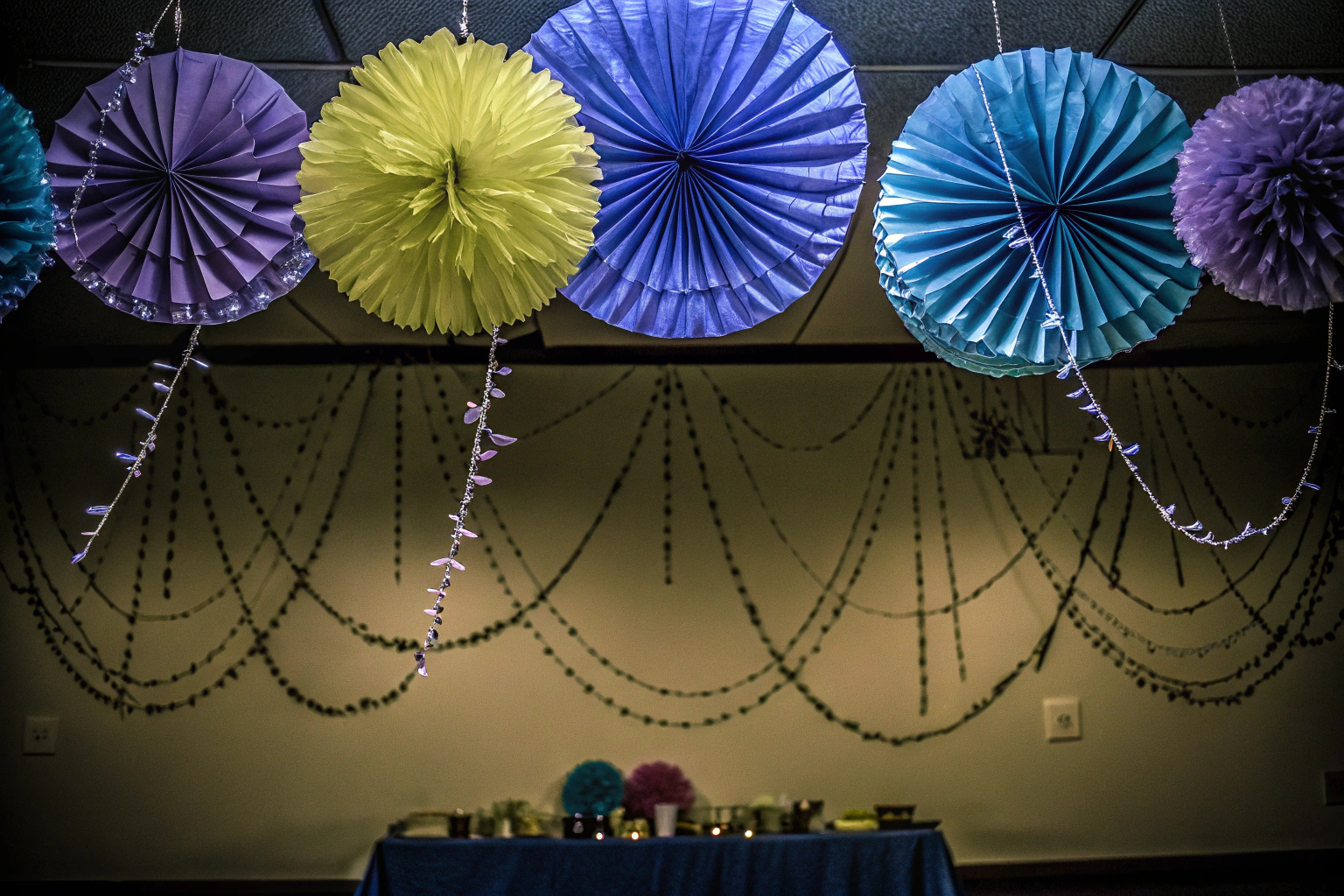 Bunte Papierpompoms und Fächer, die von der Decke hängen und eine festliche Atmosphäre schaffen. Papierpompoms und Fächer Dekoration