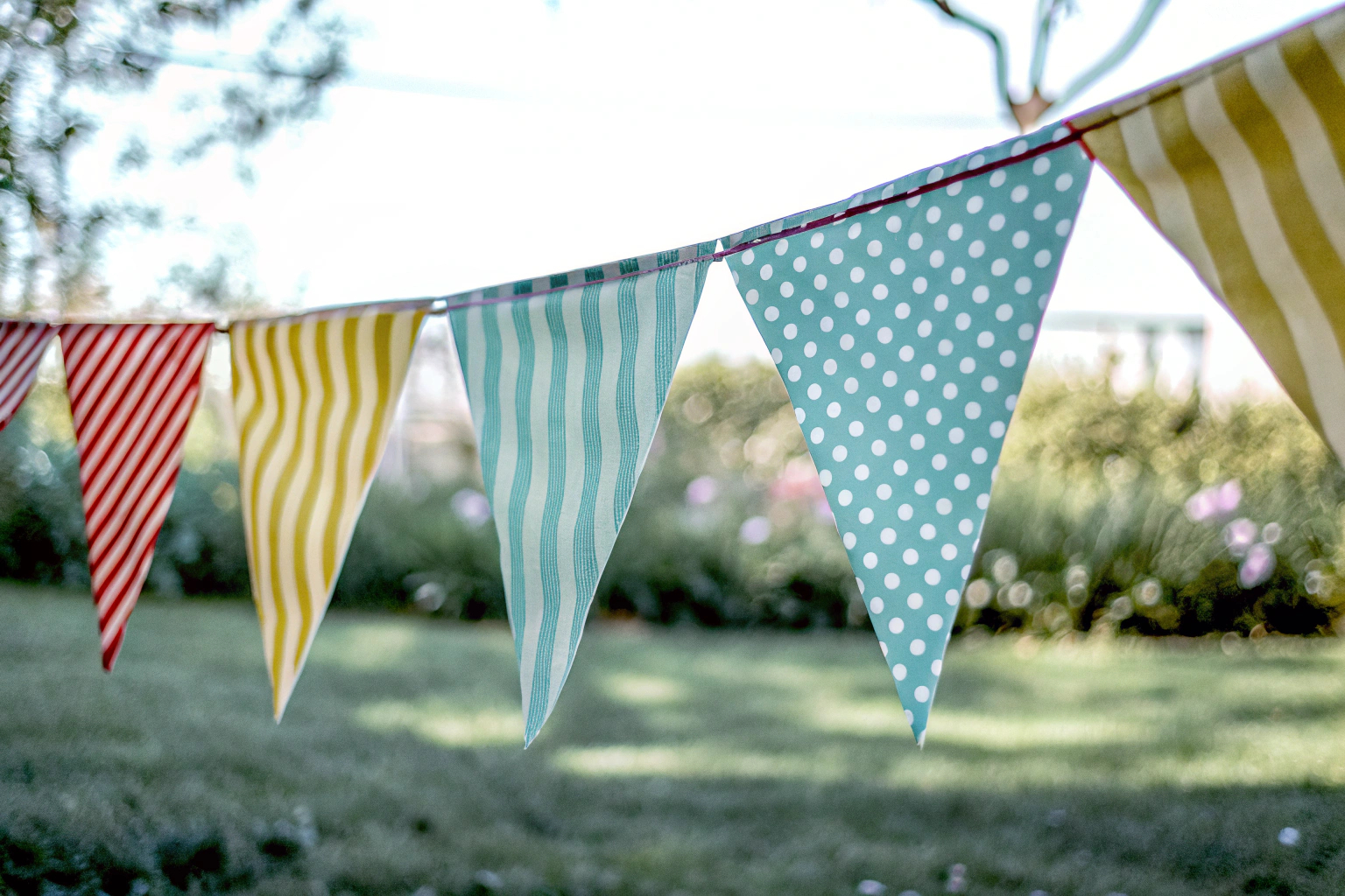 Detailaufnahme einer bunten Wimpelkette, die über einem Garten gespannt ist. Wimpelkette im Garten