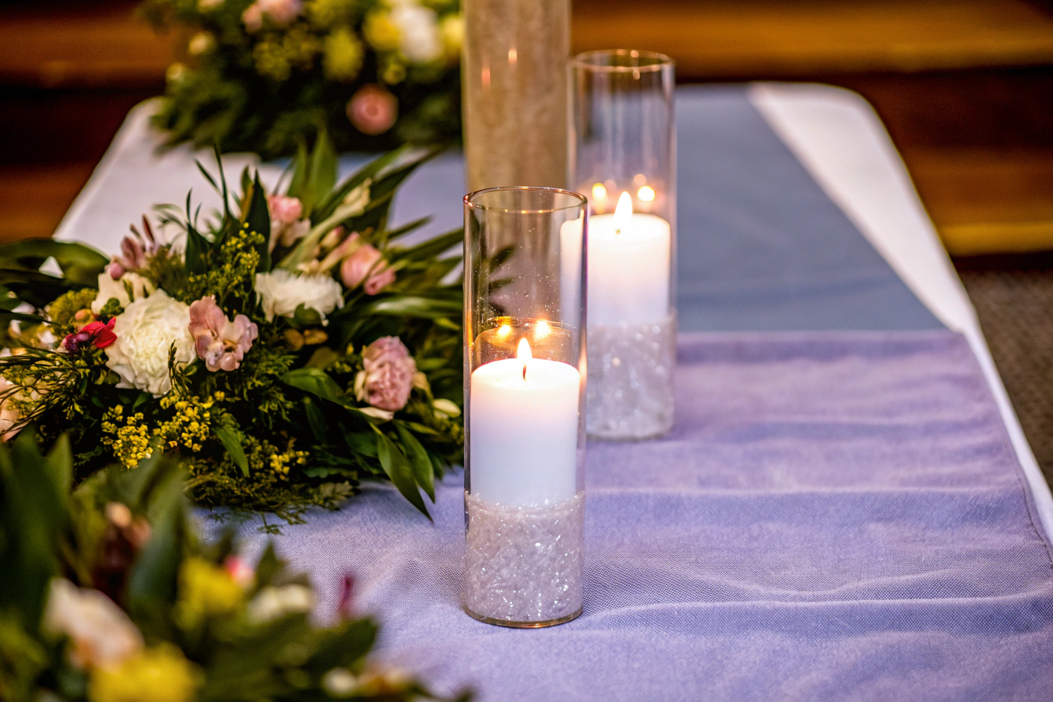 Detailaufnahme einer festlich gedeckten Tafel mit Vlies-Tischläufer, Kerzen und Blumenarrangements. Festlich gedeckte Tafel mit Vlies-Tischläufer