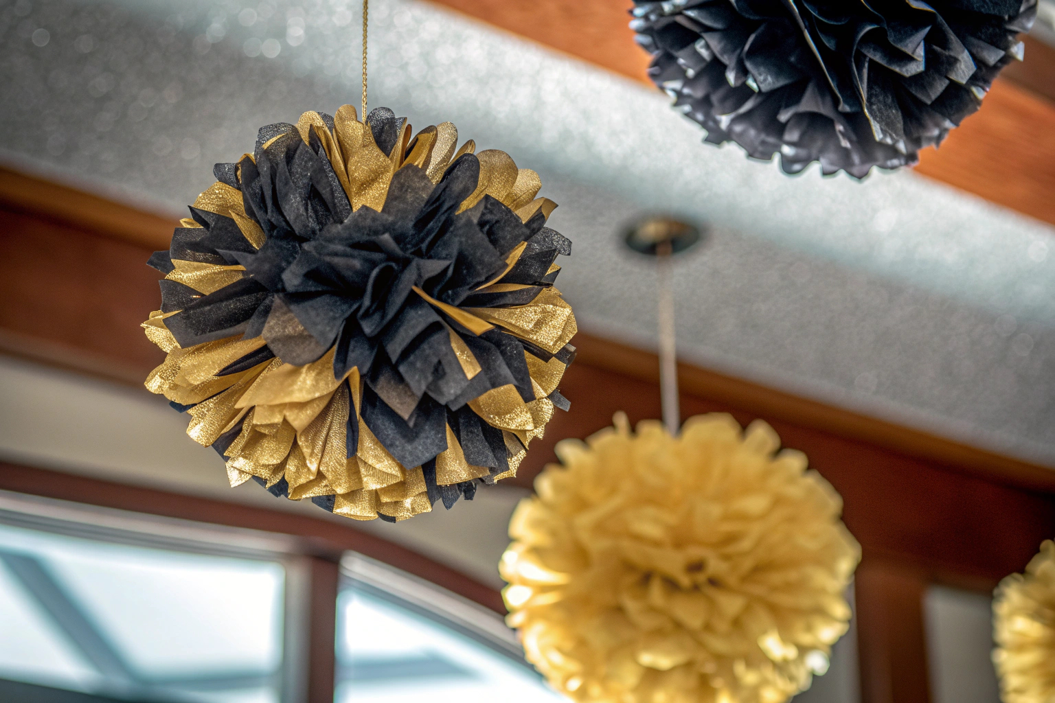 Detailaufnahme von eleganten Pompons in Schwarz und Gold, die an der Decke hängen. Schwarz-Gold Pompons Deko