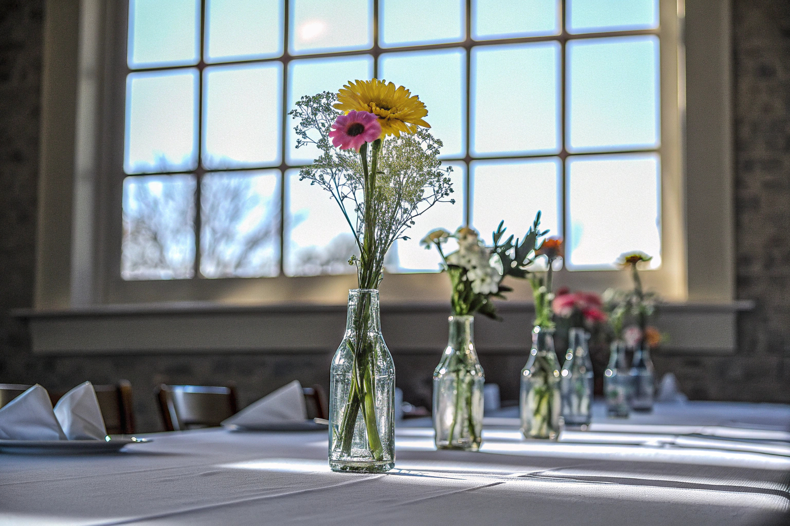 Ein Arrangement aus kleinen Glasvasen mit Blumen, das auf einem Tisch dekoriert ist. Kleine Glasvasen als Tischdekoration