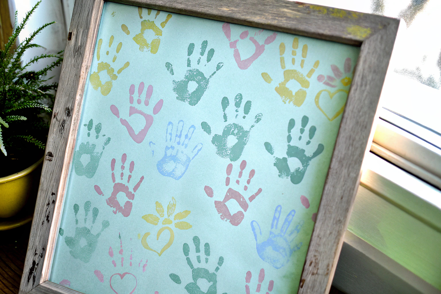 Ein Familienhandabdruck-Kunstwerk mit bunten Handabdrücken in einem dekorativen Holzrahmen. Familienhandabdruck-Kunstwerk