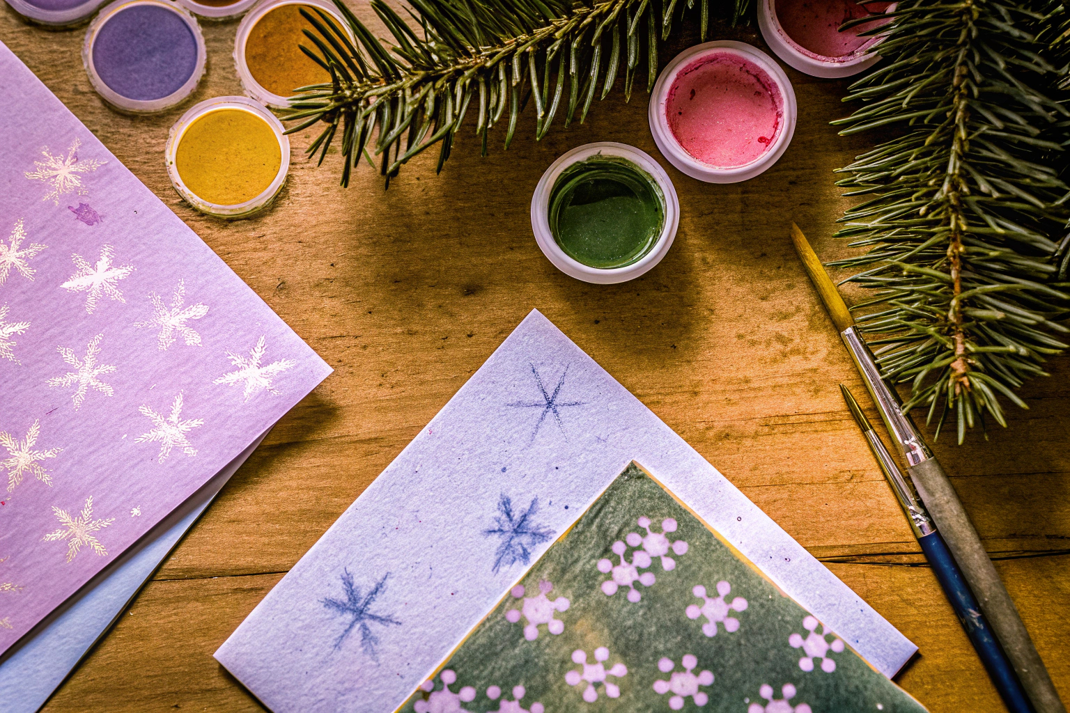 Eine Auswahl an Bastelmaterialien für Weihnachtskarten, darunter Aquarellfarben, Pinsel und recyceltes Papier. Bastelmaterialien für Weihnachtskarten