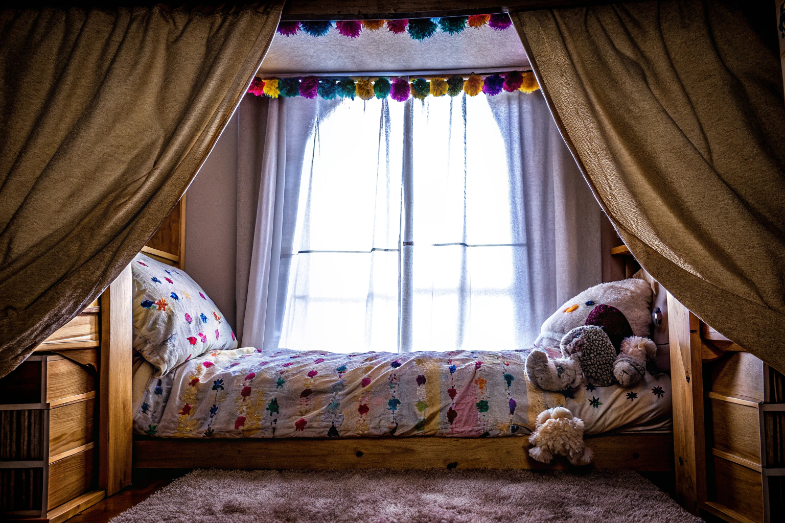Eine bunte Pompom-Girlande, die über einem Kinderbett hängt. Bunte Pompom-Girlande im Kinderzimmer