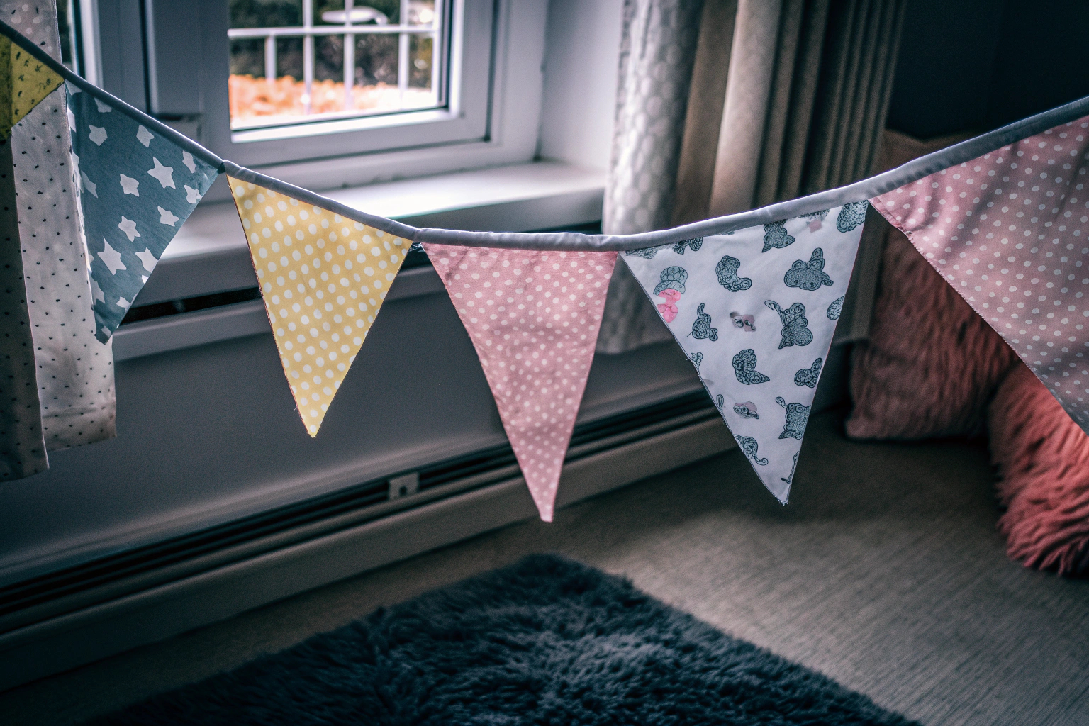 Eine bunte Stoffwimpelkette, die in einem Kinderzimmer hängt und eine fröhliche Atmosphäre schafft. Bunte Stoffwimpelkette im Kinderzimmer