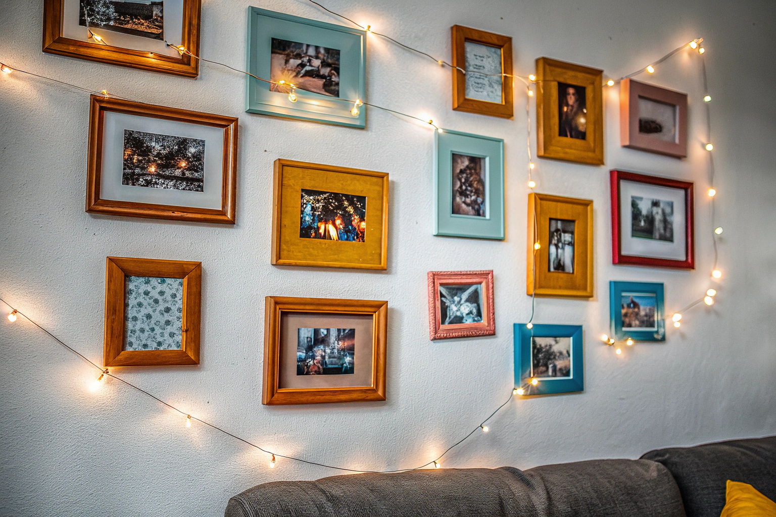Eine kreative Fotowand in einem Wohnzimmer, die mit Lichterketten und Fotos dekoriert ist. Kreative Fotowand im Wohnzimmer