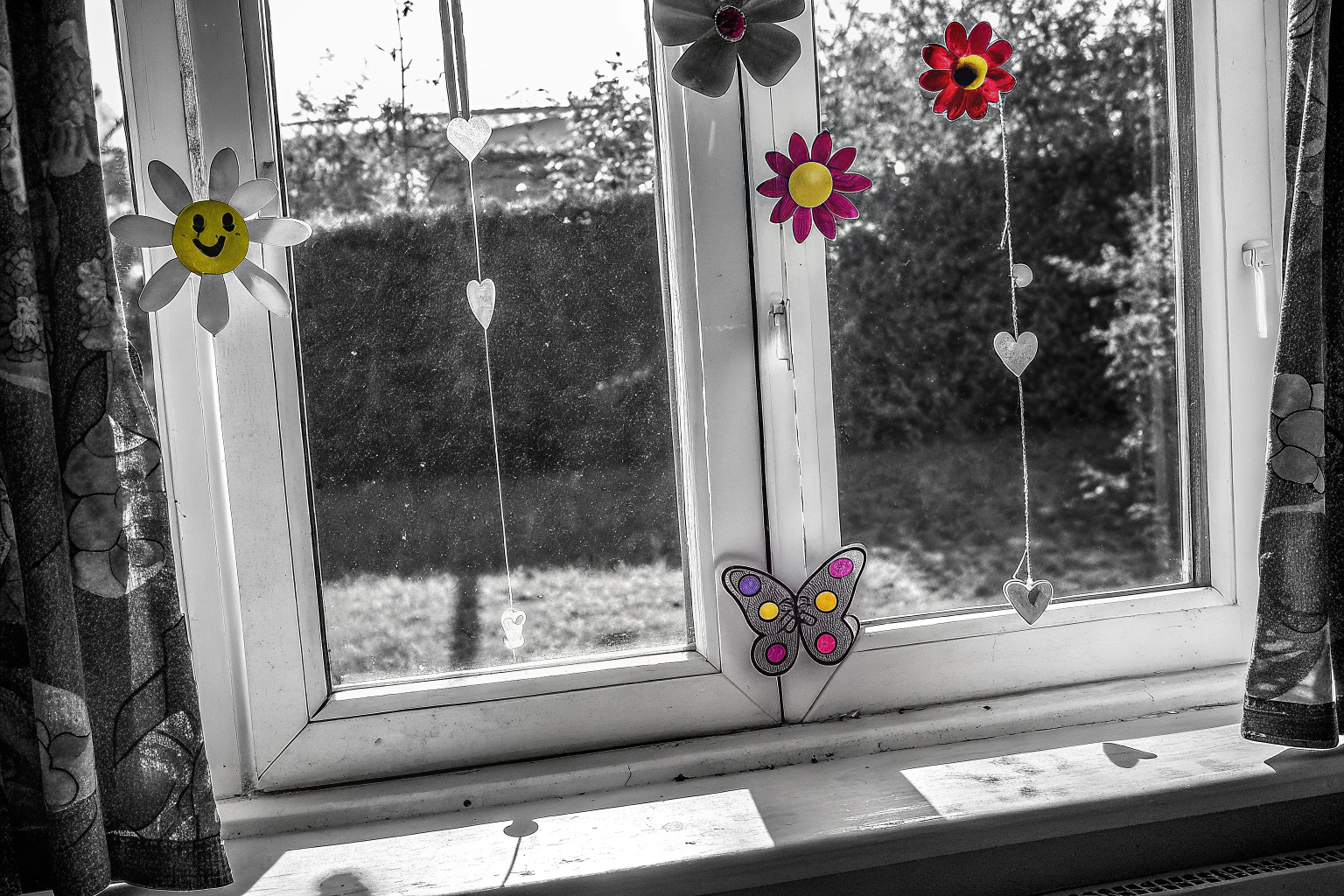 Fensterbilder mit frühlingshaften und sommerlichen Motiven auf einem Fenster, das von der Sonne beschienen wird. Fensterbilder mit Blumenmotiven